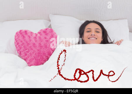 Composite image of woman lying in bed next to a fluffy heart pillow Stock Photo