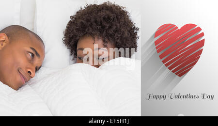 Composite image of happy couple lying in bed under the duvet Stock Photo