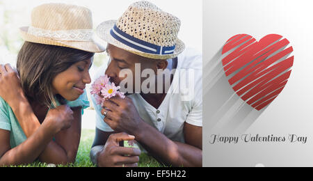 Composite image of happy couple lying in garden together smelling flowers Stock Photo
