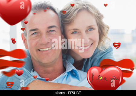 Composite image of smiling woman hugging her husband on the couch from behind Stock Photo