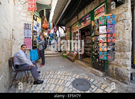 A man is sitting outside his shop on the Via Dolorosa, one of the small streets in the old city of Jerusalem Stock Photo