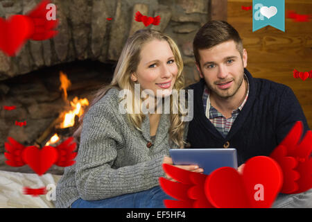 Composite image of couple using tablet pc in front of lit fireplace Stock Photo