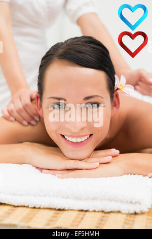 Composite image of peaceful brunette enjoying a herbal compress massage smiling at camera Stock Photo