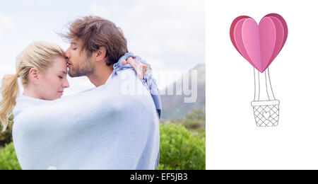Composite image of cute affectionate couple standing outside wrapped in blanket Stock Photo