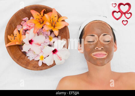 Composite image of smiling brunette getting a mud treatment facial beside bowl of flowers Stock Photo