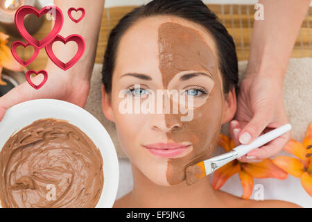 Composite image of peaceful brunette getting a mud facial applied Stock Photo