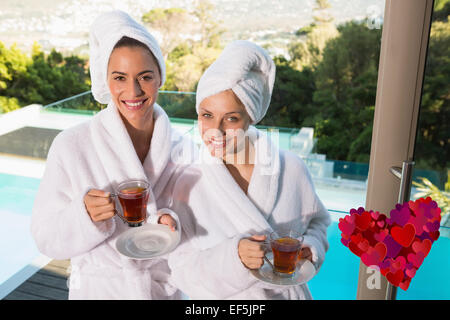Composite image of smiling women in bathrobes having tea Stock Photo