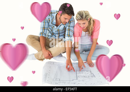 Composite image of attractive young couple sitting looking at blueprint Stock Photo