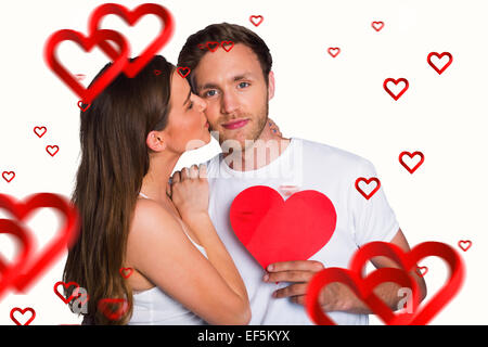 Composite image of woman kissing man as he holds heart Stock Photo