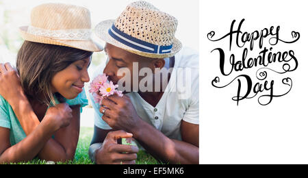 Composite image of happy couple lying in garden together smelling flowers Stock Photo