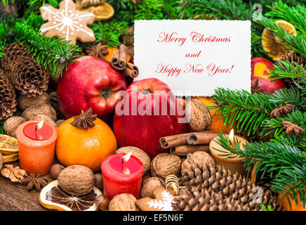 Christmas decoration with burning candles and greetings card. Fruits, nuts, spices and cookies Stock Photo