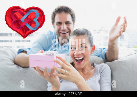 Composite image of man surprising his delighted girlfriend with a pink gift on the sofa Stock Photo