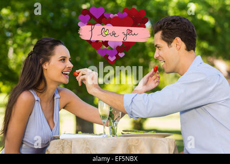 Composite image of couple feeding strawberries to each other at outdoor cafÃ© Stock Photo