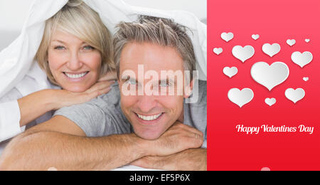 Composite image of couple smiling under the covers Stock Photo