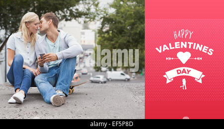 Composite image of cute young couple sitting on skateboard kissing Stock Photo