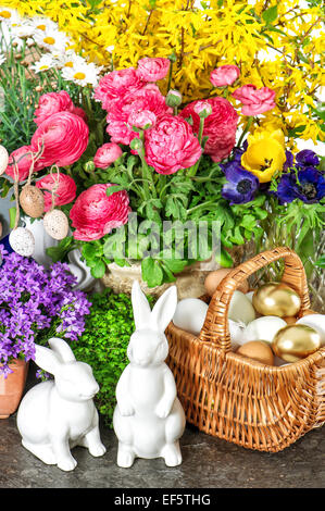 Easter decoration with spring flowers, golden eggs and bunnies. Forsythia and ranunculus blossoming Stock Photo