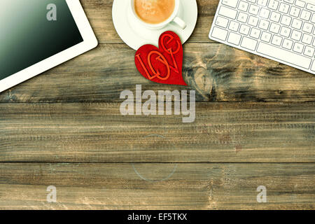 Red love heart, tablet pc, keyboard and coffee on wooden table. Valentines Day workplace. Retro style toned picture Stock Photo