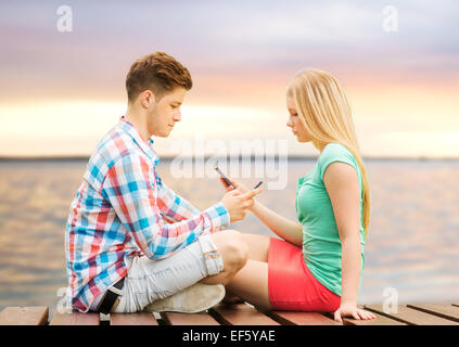 couple with smartphones sitting on bench Stock Photo