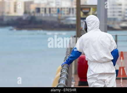 Council worker in protective suit and mask using chemical product to clean Stainless steel railings overlooking beach in Spain Stock Photo