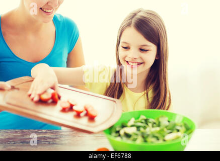 little girl with mother adding tomatoes to salad Stock Photo