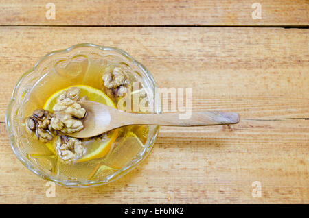 Small dish filled with honey, lemon slices and walnuts on a wooden table Stock Photo