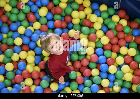 A little boy (2 1/2 years old) sat in coloured balls looking up and smiling at the camera