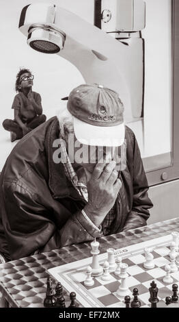 Elderly Spanish man playing chess in park  with advert for bathroom fittings in background Stock Photo