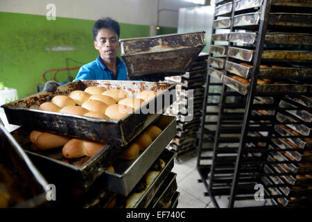 Young man in a bakery taking bread out of the oven, Gampong Nusa, Aceh province, Indonesia Stock Photo