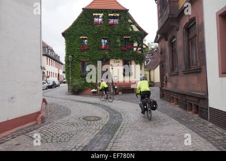 Two cyclists on tour cycling through cobbled streets of Walluf, Germany. Stock Photo