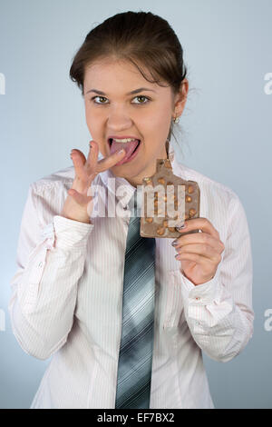 young business woman wearing business shirt and tie holding chocolate and licking finger Stock Photo