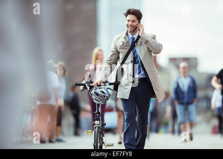 Businessman talking on cell phone pushing bicycle in city Stock Photo