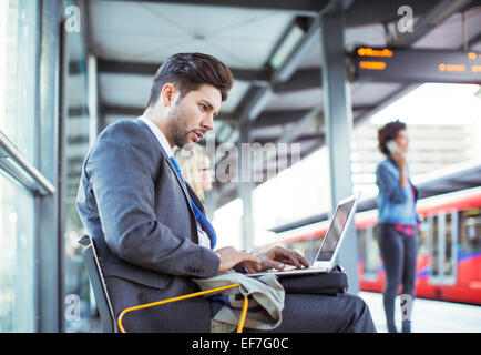 Businessman using laptop at train station Stock Photo