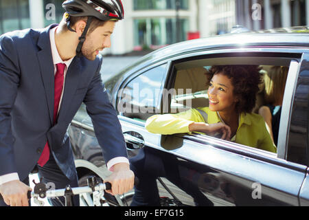 Businessman on bicycle talking to woman in car Stock Photo