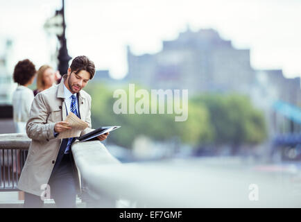 Businessman reading newspaper on urban waterfront Stock Photo