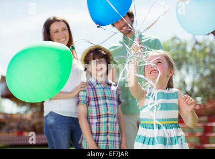 Young girl holding bunch of balloons, family standing behind her Stock Photo