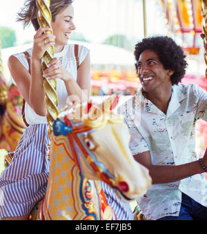 Young multiracial couple smiling on carousel in amusement park Stock Photo