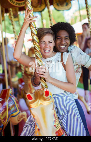 Young multiracial couple smiling on carousel in amusement park Stock Photo