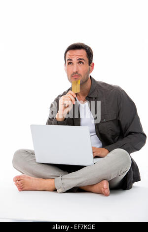 Thoughtful man sitted on the floor holding credit card and buying online Stock Photo