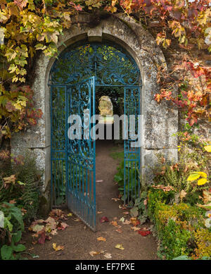 Wrought-iron gate set in a Cotswold stone arch and framed by vine leaves displaying autumnal hues at Rousham House, Oxfordshire, England Stock Photo