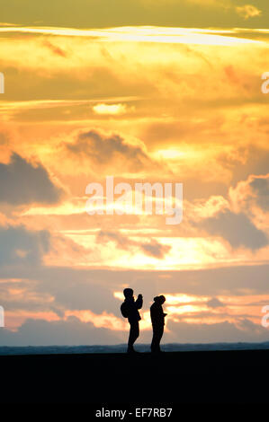 Aberystwyth, Wales, UK. 28th January, 2015. UK Weather: Two walkers are silhouetted against a vivid sunset on a stormy day in Aberystwyth Wales. Much of northern England and Scotland are under 'amber' alert as heavy snow and freeezing winds are forecast for ther next 24 hours. Credit:  keith morris/Alamy Live News Stock Photo