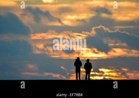 Aberystwyth, Wales, UK. 28th January, 2015. UK Weather: Two walkers are silhouetted against a vivid sunset on a stormy day in Aberystwyth Wales. Much of northern England and Scotland are under 'amber' alert as heavy snow and freeezing winds are forecast for ther next 24 hours. Credit:  keith morris/Alamy Live News Stock Photo