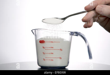 Man pours a spoonful of sugar into a measuring cup. Stock Photo
