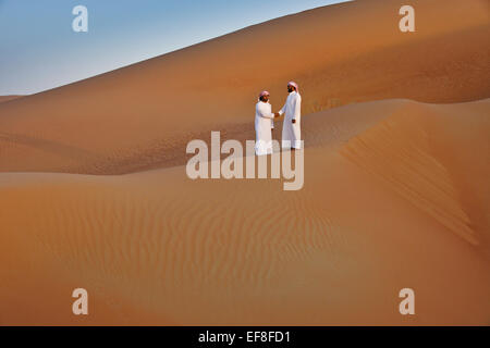 Arab men in traditional dress amid sand dunes of Liwa, Abu Dhabi, UAE Stock Photo