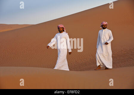 Arab men in traditional dress amid sand dunes of Liwa, Abu Dhabi, UAE Stock Photo