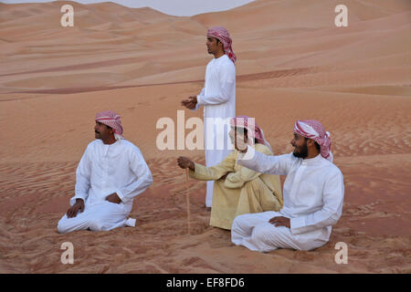 Arab men in traditional dress amid sand dunes of Liwa, Abu Dhabi, UAE Stock Photo