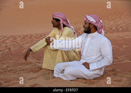 Arab men in traditional dress sitting in sand dunes of Liwa, Abu Dhabi, UAE Stock Photo