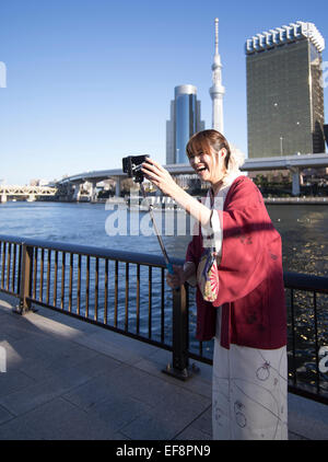 Japanese woman using a selfie stick to take a selfie on the banks of the Sumida River, Asakusa, Tokyo. Tokyo Skytree in the back Stock Photo