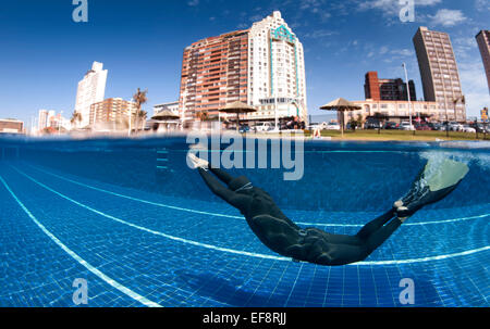 South Africa, KwaZulu Natal, Durban, Man wearing monofin diving in swimming pool with beachfront hotels in background Stock Photo