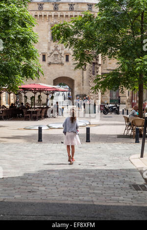 A little girl on a scooter rides towards Calihau Gate, historic architecture in Bordeaux France. Stock Photo