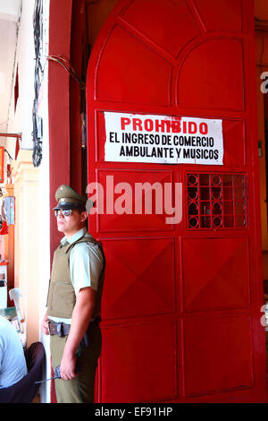 Policeman standing next to entrance to market and sign prohibiting the entry of street vendors, informal traders and musicians, Iquique, Chile Stock Photo